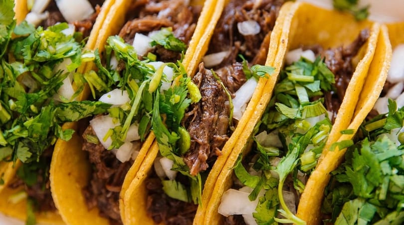 Close-up of several street tacos filled with shredded meat, diced onions, and cilantro.