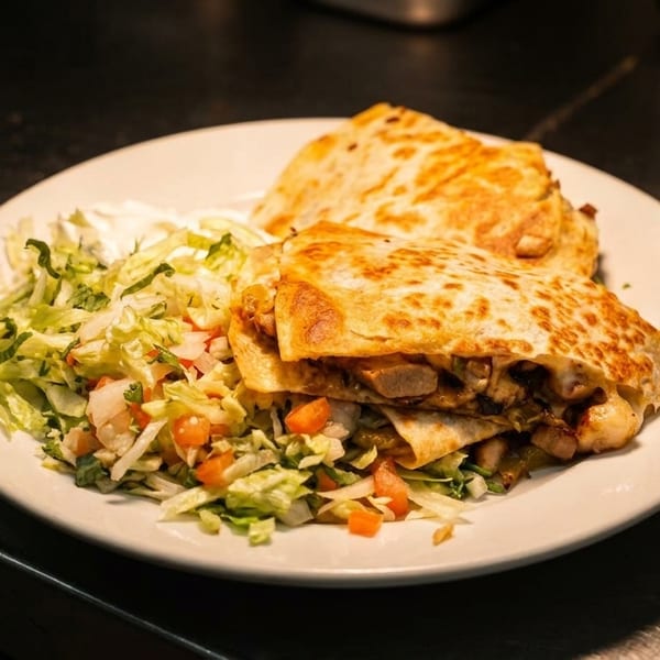 Two golden-brown quesadillas filled with chicken and vegetables, served with shredded lettuce and pico de gallo.