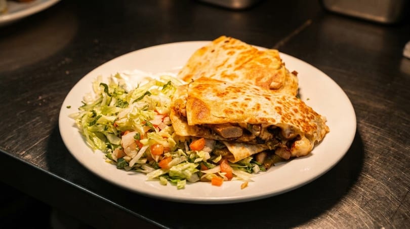 Two golden-brown quesadilla halves filled with meat and vegetables, served with shredded lettuce and pico de gallo.