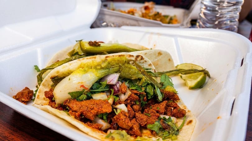 Two tacos with meat, cilantro, onions, and green chiles in a white takeout container.